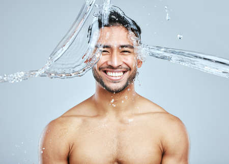 Splashing some freshness all over him. Studio portrait of a handsome young man splashing water on his face against a grey background.の写真素材