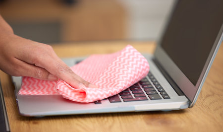 Getting in the crevices. Shot of a woman cleaning the dust from the laptop keyboard.の写真素材