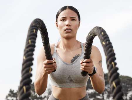 Work hard, stay consistent and be patient. Shot of an athletic young woman doing heavy rope training outside.の写真素材
