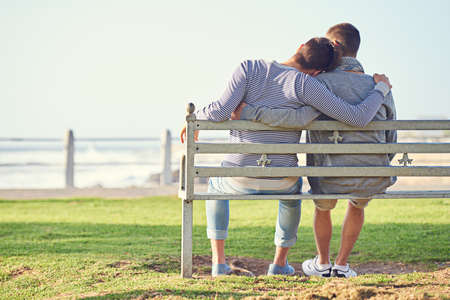 Taking in a romantic afternoon. Rearview shot of a young gay couple sitting together on a park bench.の写真素材