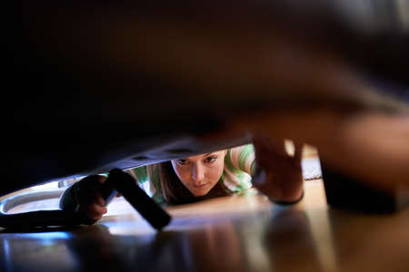 She never misses a spot. Shot of a young woman vacuuming underneath a piece of furniture.
