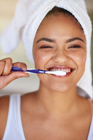 Healthy teeth are happy teeth. Portrait of a happy and attractive young woman brushing her teeth.の写真素材