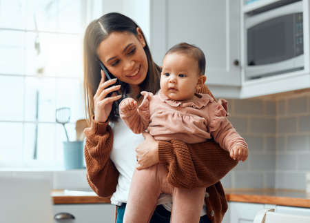 Balancing being a mother and businesswoman. Cropped shot of an attractive young woman carrying her newborn baby while working at home.の写真素材