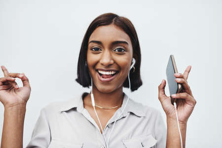 Always bring your best side out. Studio portrait of a young creative businesswoman listening to music on her cellphone against a grey background.の写真素材