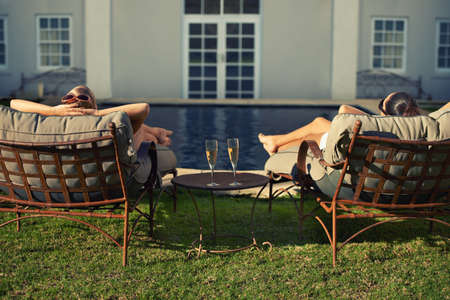 Enjoying the high life. Rear view of two young woman relaxing on loungers facing the pool.の写真素材
