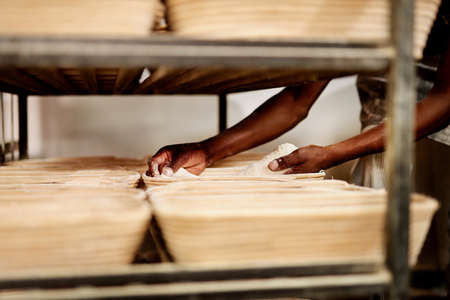 Im getting my first batch ready for the oven. Cropped shot of a male baker placing dough on a baking trolley.の写真素材