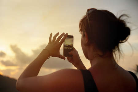 I cant wait to share this view. Shot of a young woman photographing a tropical view with her...