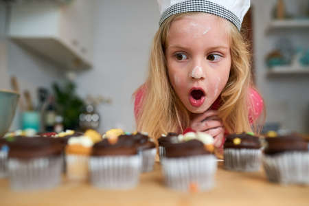 My first batch of cupcakes. Shot of a surprised little girl looking at cupcakes she baked at home.の写真素材