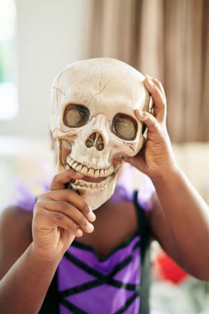 Taking my face off. Shot of an unrecognizable little child covering their face with a skull.