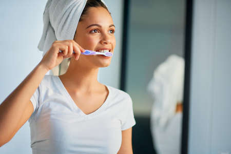 Welcome a new day with fresh breath. Shot of an attractive young woman brushing her teeth at home.の写真素材
