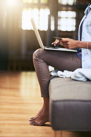 Nothing beats the convenience of credit. Cropped shot of a woman using a laptop and credit card on the sofa at home.の写真素材