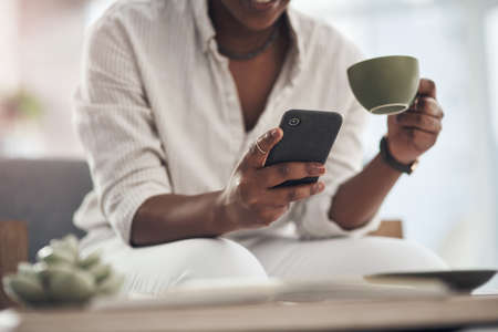 Start your day the serene way with tea. Shot of a businesswoman using her smartphone to send text messages while drinking coffee.の写真素材