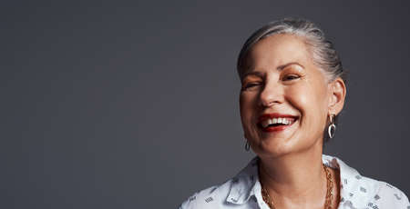 Keep the good times rolling. Studio shot of a senior woman sitting on a chair against a grey...
