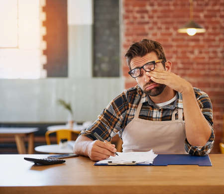 This admin will be the end of me. Shot of an exhausted young business owner doing admin at a table...
