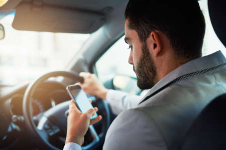 Distracted driving can increase the chance of a road accident. Cropped shot of a man using his phone...