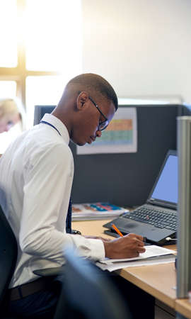 Busy making success happen as he does. Shot of a young businessman working at his desk in an office.
