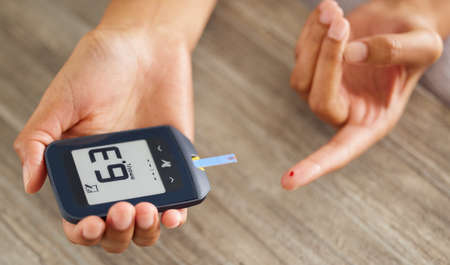 A touch higher than ideal. High angle shot of an unrecognizable woman testing her blood sugar level at home.の写真素材