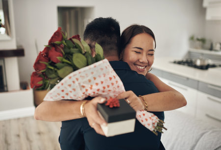 Random acts of kindness. Shot of a young man surprising his wife with flowers at home.の写真素材