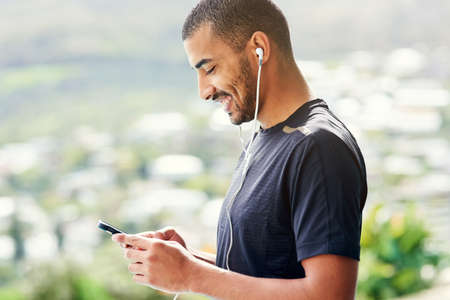 Setting the perfect playlist to get him motivated. Cropped shot of a young sporty man checking his...
