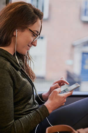Checking the bus routes online. Cropped shot of an attractive young woman listening to music while...