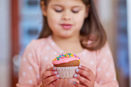 Take a look at my delicious dessert. Cropped shot of a little girl looking at a cupcake in her hands.の写真素材