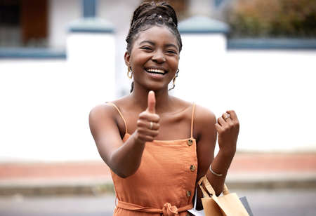 I shop, therefore I am. Shot of a young female and showing a thumbs up sign in the city.の写真素材