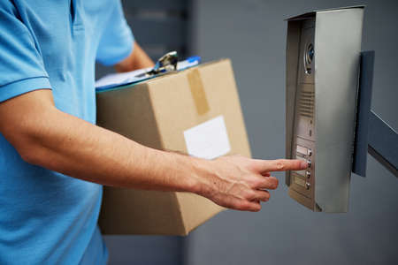 Your package has arrived. Closeup shot of a courier ringing an intercom while making a delivery.の写真素材