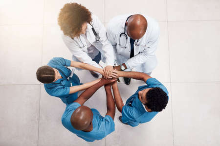 Lets get this day started. High angle shot of a group of young doctors forming a huddle with their hands inside of a hospital during the day.の写真素材