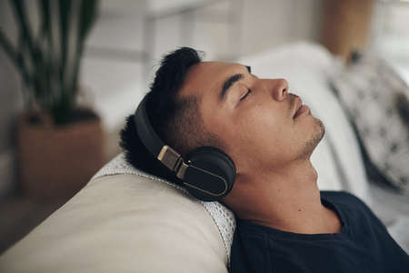 When my headphones are in, the world is blocked out. Shot of a young man using headphones at home.の写真素材