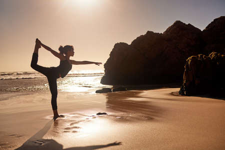 Yoga will change your life for the better. Shot of a young woman practicing yoga at the beach.の写真素材