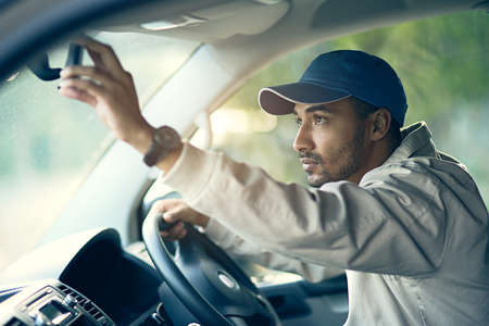Off to make his next delivery stop. Cropped shot of a delivery man adjusting the rear-view mirror of...
