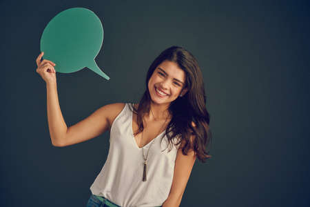 I mean what I say. Studio shot of a cheerful young woman holding up a speech bubble while standing...