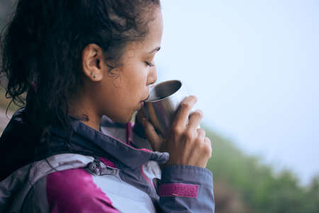 Coffee breaks are needed on early morning hikes. Cropped shot of an attractive young woman drinking coffee while taking a break during her early morning hike.の写真素材