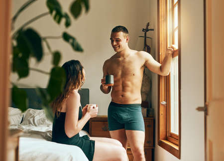Start the day with your favourite person. Shot of a happy young couple having their morning coffee together in the bedroom at home.の写真素材