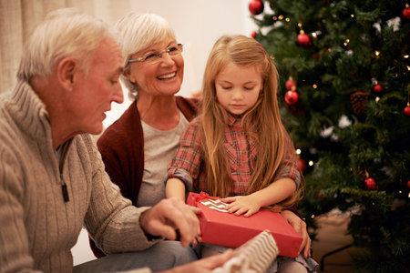 I wonder whats in this one. Shot of a little girl spending Christmas with her grandparents.の写真素材