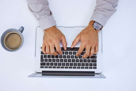 Coffee got me through this lengthy e-mail. Cropped shot of an unrecognizable businessman using his laptop while sitting at his desk.の写真素材