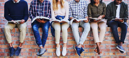 Studying on campus. Cropped shot of a group of unrecognizable university students studying while sitting outside on a facebrick wall.の写真素材