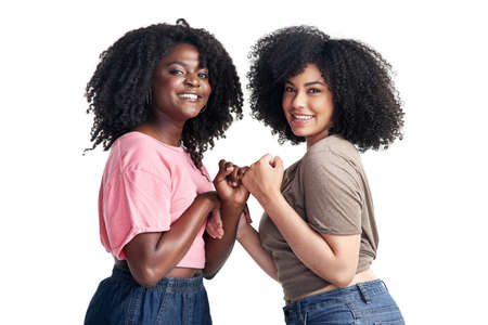Stuck together like glue, just me and you. Studio shot of two young women linking their fingers against a white background.の写真素材