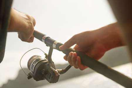 Time to reel it in. Cropped shot of an unrecognizable young man fishing while out at sea on his...