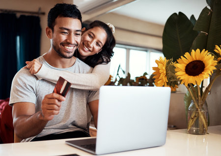 Theres a massive discount on that holiday we wanted to go on. Shot of a man holding a credit card and using his laptop while at home with his girlfriend.の写真素材