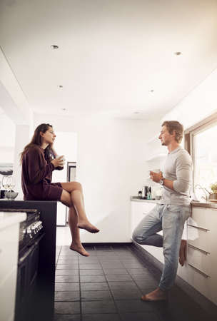 Mornings at home make the best coffee dates. Shot of a happy young couple enjoying a relaxing cup of coffee together in the kitchen.の写真素材