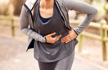 Runners know this pain all too well. Shot of an unrecognisable woman experiencing stomach ache while...
