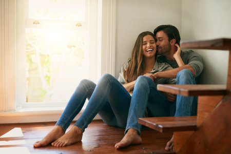We are both the same in every way. Shot of an affectionate young couple sitting in a corner and holding each other.の写真素材