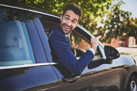 Im on my way to work buddy. Shot of a cheerful young businessman hanging out of a car window and pointing with his hand towards the front of his car.の写真素材