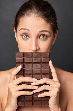 Shes a lover of chocolate. Studio shot of an attractive young woman being tempted by something sweet.の写真素材