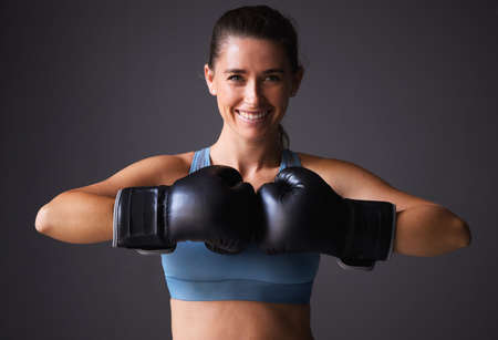 Wanna see how much power are in my punches. Portrait of a young woman wearing boxing gloves against a grey background.の写真素材