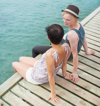 Sharing a quiet moment together. A high angle shot of a young couple talking while sitting on a dock with their legs hanging over the edge.の写真素材