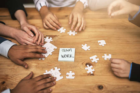 Planning it all out, piece by piece. High angle shot of a group of unrecognizable coworkers building a puzzle on their boardroom table.の写真素材