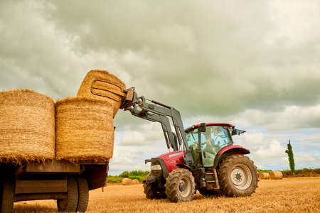 Stacking those hay bales. Shot of a farmer stacking hale bales with a tractor on his farm.の写真素材