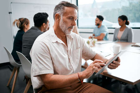 Making sure he misses nothing. Cropped shot of a handsome mature businessman attending a meeting in the boardroom with his colleagues in the background.の写真素材